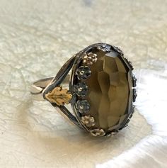 "Commitment Pretty handmade smoky quartz ring. A yellow gold leaf element is soldered to both sides of the floral bezel.(R2554). © 2011-2015, Artisanimpact Inc. All rights reserved. Construction & Dimensions: Sterling silver, 10k yellow gold, smoky quartz Approximate top size: 17mm (0.66in) x 12mm (0.47\") We can make any size, including quarter sizes. Please just indicate the requested size in the order. About our jewelry Artisanlook offers an exciting collection, designed and made by artis Luxury Topaz Rings With Rose Cut Diamonds, Handmade Elegant Sterling Silver Topaz Ring, Smoky Quartz Gemstone Ring For Anniversary, Elegant Handmade Sterling Silver Topaz Ring, Smoky Quartz Gemstone Jewelry For Wedding, Elegant Smoky Quartz Gemstone Rings, Elegant Smoky Quartz Rings For Anniversary, Wedding Smoky Quartz Gemstone Jewelry, Elegant Smoky Quartz Jewelry For Weddings