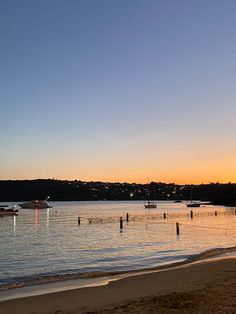 boats are floating in the water at sunset on a beach with sand and trees around it