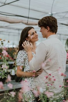 a man and woman standing in a greenhouse looking at each other's eyes while holding flowers