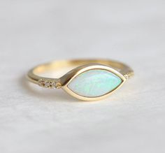 a gold ring with an opal and diamonds on the side, sitting on a white surface