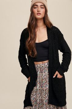 a woman in a black cardigan and floral skirt is standing with her hands on her hips