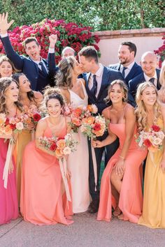 a group of people standing next to each other in front of flowers and bushes with their hands up