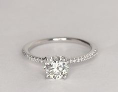 a white gold engagement ring with diamonds on the band and a single round diamond in the center