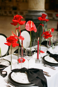 the table is set with red flowers and place settings