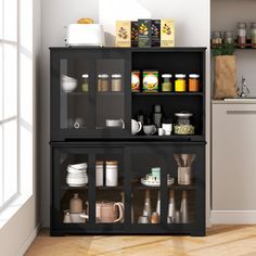 a kitchen with white walls and wooden flooring next to an open cabinet filled with dishes