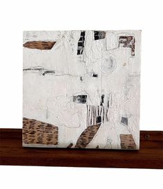 an abstract painting with white and brown colors on a wooden shelf next to a wall