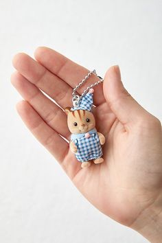 a hand holding a tiny toy animal wearing a blue and white checkered shirt on it's chest