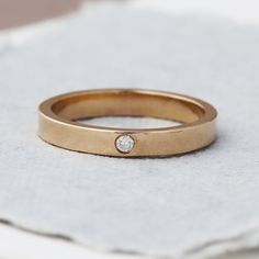 a gold wedding band with a diamond on the top, sitting on a piece of cloth