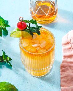 two glasses filled with drinks sitting on top of a blue table next to limes