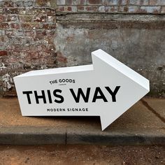 a white sign that says the goods is this way and has an arrow on it