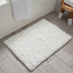 a white bathroom rug on the floor next to a bath tub and toilet paper roll