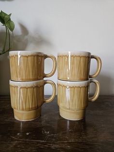 three coffee mugs sitting next to each other on top of a wooden table with a plant in the background