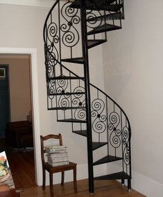 a spiral staircase in the corner of a room next to a chair and table with books on it