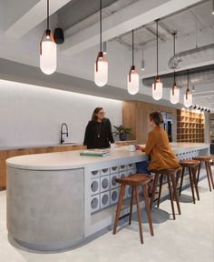 two women are sitting at the counter in an office with lights hanging from the ceiling