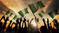 many people raising their hands in the air with green and white flags flying above them