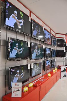 televisions are on display in a store with red and white shelves holding tennis memorabilia