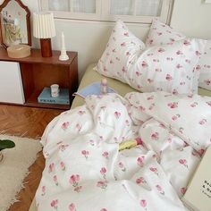 a bed with white sheets and pink flowers on it, next to a bookcase