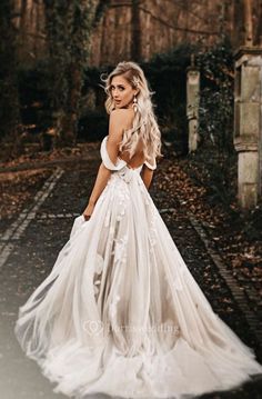 a woman in a white wedding dress standing on a path with her back to the camera