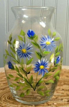 a glass vase with blue flowers painted on the inside and green leaves in the outside