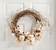 a wreath with white flowers and leaves hanging on the front door to decorate it for fall