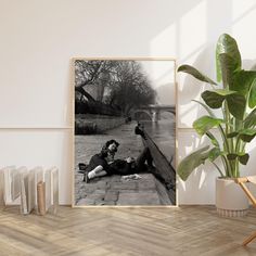 a black and white photo of a woman laying on the ground next to a potted plant