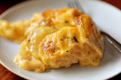 a white plate topped with chicken and cheese covered in gravy next to a fork