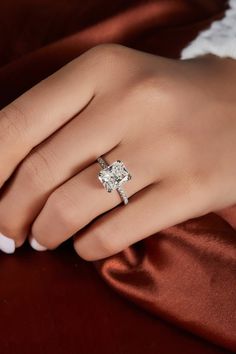 a woman's hand with a diamond ring on top of her finger and red satin