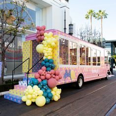 a pink and yellow bus with balloons on the side