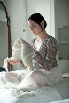 a woman sitting on top of a bed holding a fan