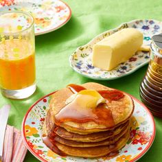 pancakes with butter and syrup on them sitting on a green tablecloth next to orange juice