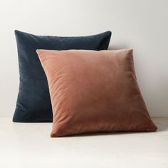 two velvet pillows sitting on top of a white table next to each other, one in blue and the other in pink