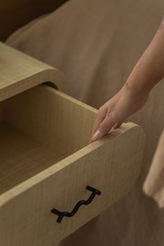 a person's hand reaching into an open drawer on a wooden bed with brown sheets