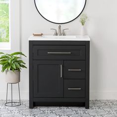 a bathroom vanity with a round mirror above it and a plant on the floor next to it