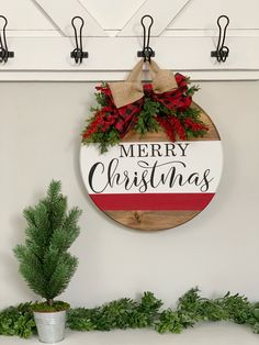 a merry christmas sign hanging on the wall next to a potted plant and pine cones