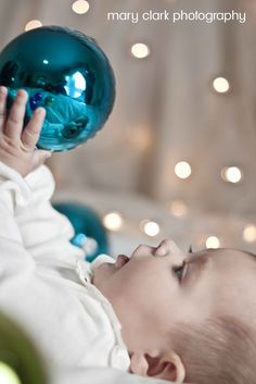 a black and white photo of a baby chewing on a blue glass ornament