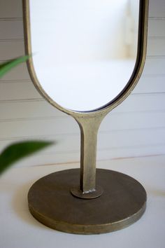 a mirror sitting on top of a metal stand next to a green potted plant