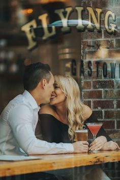 a man and woman sitting at a table in front of a bar kissing each other