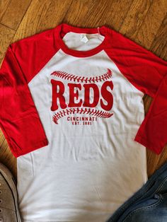 Perfect for opening day and all season long.  Show your Cincinnati Reds pride with this adorable shirt.  3/4 sleeves raglan works well in any weather.   *Unisex sizing.  Bella + Canvas brand shirt Care instructions for washing- Please wash inside out with cold water and tumble dry on low or line dry. Please do not use an iron directly on the design to protect the design quality. Material and additional information- This unisex 3/4 sleeve raglan shirt is made of 52% cotton and 48% polyester. Sleeves have been color-matched to the crew neck collar against a contrasting body with forward shoulder seams that resist separation. Contemporary retail fit is flattering, and folks love having a label that is easy to remove. Finally, you will enjoy the soft hand of Airlume 100% combed and ringspun co Red Varsity Baseball Jersey For Fans, Red Letter Print Baseball Jersey For Sports Fans, Red Sports Fan Baseball Jersey With Letter Print, Red Letter Print Baseball Jersey For Game Day, Red Baseball Jersey With Letter Print For Game Day, Red Varsity Baseball Jersey For Game Day, Collegiate Red Baseball Jersey For Baseball Season, Red Baseball Jersey For Fan Gear With Team Spirit, Red Baseball Jersey For Team Spirit