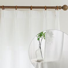 a vase with a plant in it sitting next to a mirror on a table near a curtain