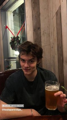 a young man sitting at a table with a glass of beer in front of him