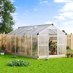 a small greenhouse in the middle of a green yard with potted plants and flowers