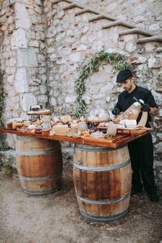 a man sitting at a table with food on top of it next to two wine barrels