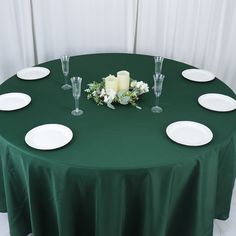 a green table cloth with white plates and flowers on it is set up for a formal function