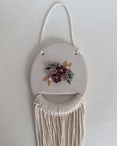 a white wall hanging with flowers and tassels attached to it's side