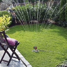 a garden with water sprinkles in the grass and a lawn chair next to it