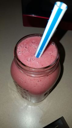 a pink smoothie in a mason jar with a blue striped straw