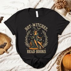 Thank you for visiting SuniDazeDesigns and supporting a small family owned business.  Embrace your inner bookworm with our retro Halloween shirt, featuring a vintage-inspired design of a witch engrossed in a spellbinding read. Perfect for those who know that intelligence is the ultimate enchantment, this 'Hot Witches Read Books' tee combines spooky style with a love for literature. Show off your bewitching charm and passion for reading this Halloween season. Please carefully read the following... HOW TO ORDER  Choose Your Size Choose Your Shirt Color Select the quantity Click Add To Cart For multiple items go back to the listing and repeat the steps. PLEASE MAKE SURE YOU HAVE READ AND UNDERSTAND THE DESCRIPTION FULLY BEFORE PLACING AN ORDER PRINTING The entire process is eco-friendly; inks Black Bookish Tops With Text Print, Black Bookish Top With Text Print, Bookish Halloween Graphic Print Top, Fall Bookish T-shirt With Letter Print, Bookish Fall T-shirt With Letter Print, Bookish Graphic Print Top For Halloween, Black Bookish Top With Letter Print, Fall Themed T-shirt With Letter Print, Black Letter Print Top For Bookish Style