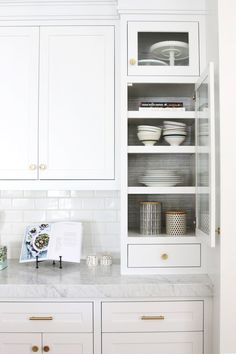 a kitchen with white cupboards and marble counter tops, gold pulls on the doors