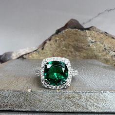 a ring with a large green stone surrounded by white diamonds on top of a rock