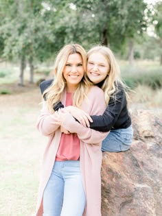 two girls hugging each other in front of a rock